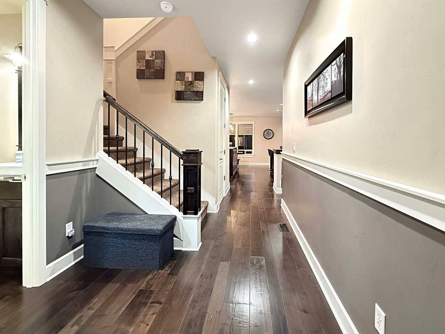 Entry hallway with engineered hardwood floors, dark wrought-iron staircase railing, board-and-batten wainscoting, and a clear sightline through the main level.